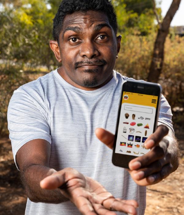 Indigenous person in the forest holds a phone displaying the Indigemoji application on it.